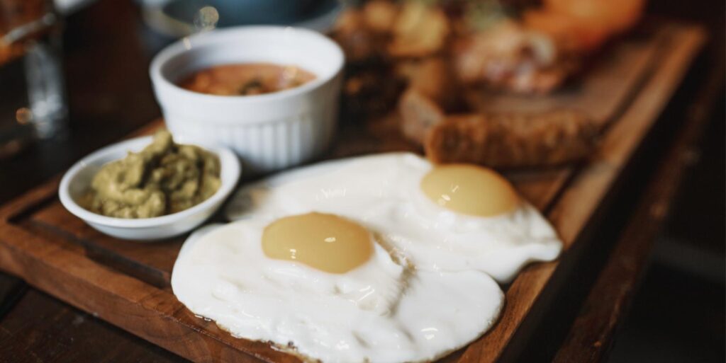 Zwei Spiegeleier mit Avocado und Dip auf einem Frühstücksbrett – Merverd frische Eier